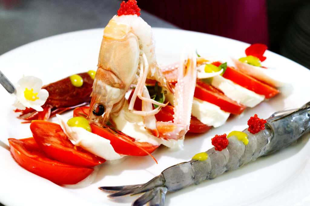 Piatto gourmet Caprese di mare con fette di pomodoro e mozzarella, scampo intero, gamberi rossi crudi e uova di pesce, specialità del ristorante La Perla del Pescatore a Desenzano del Garda.