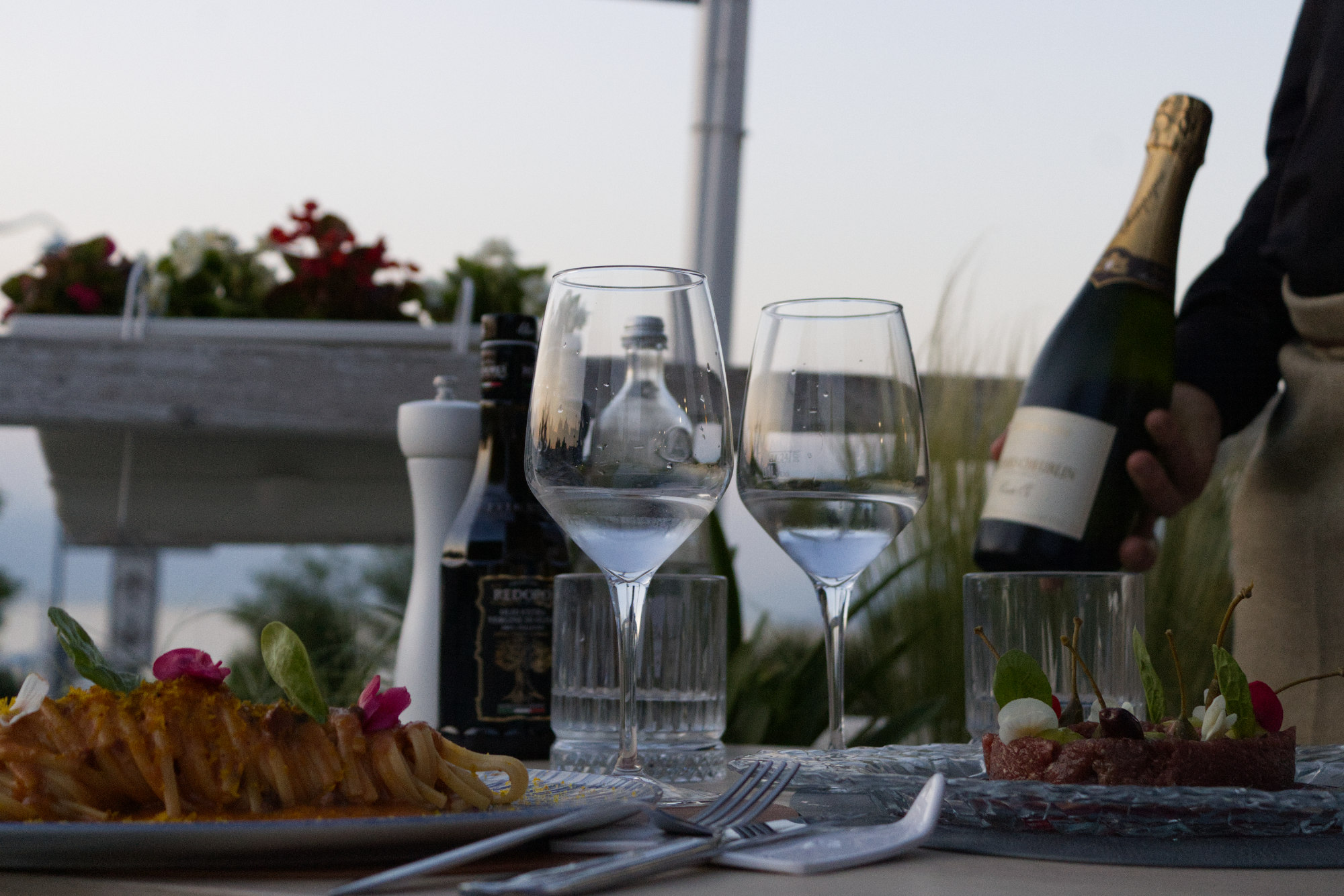 Tavolo apparecchiato all'aperto con calici di vino, primi piatti di pesce e crudité vista lago presso il ristorante La Perla del Pescatore a Desenzano del Garda.