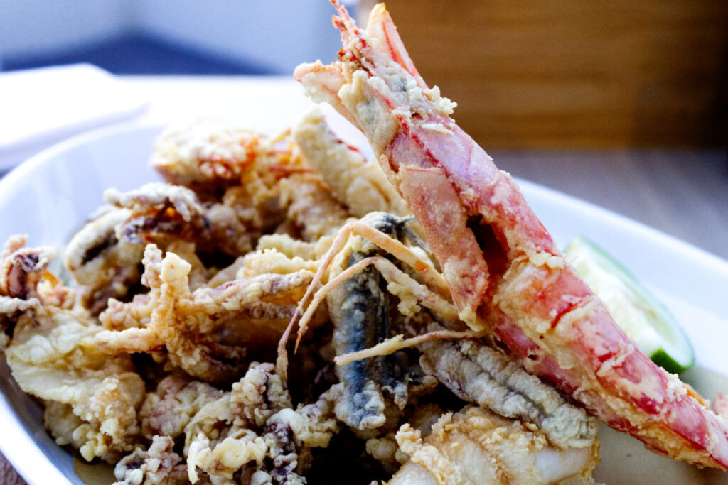 Piatto ricco di fritto misto di mare croccante con un grande gambero, ciuffi di calamari e pesciolini fritti, specialità del ristorante La Perla del Pescatore a Desenzano del Garda.