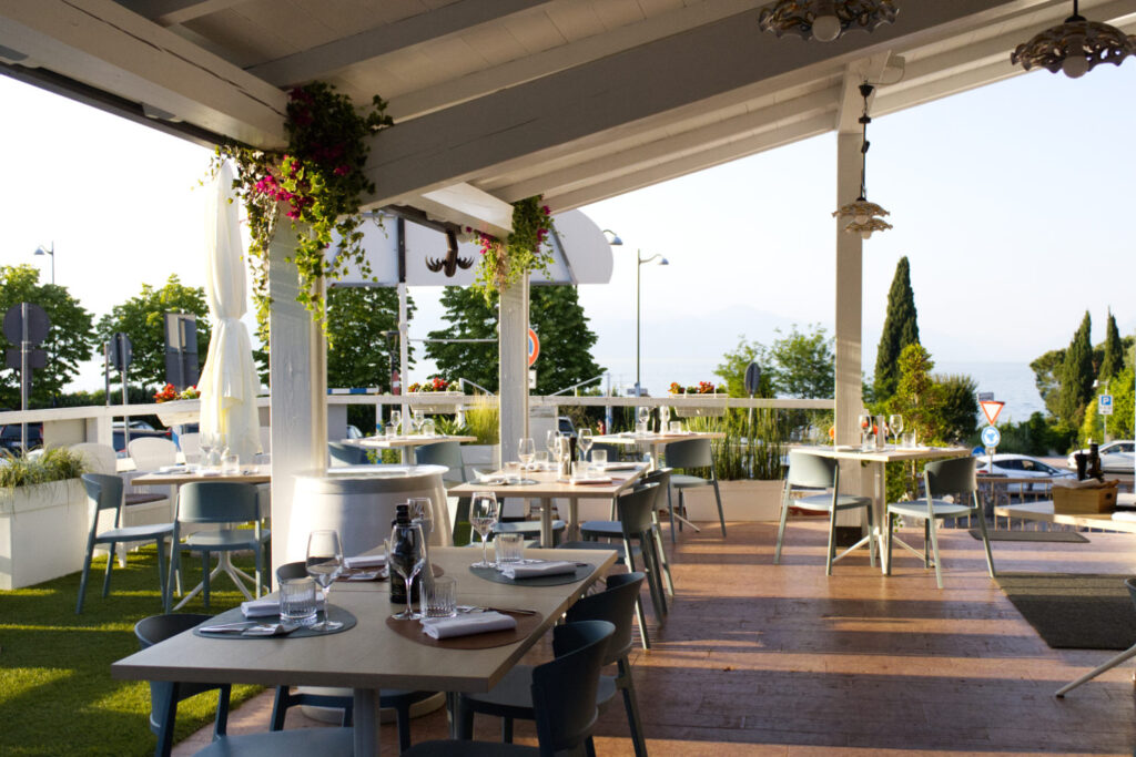 Terrazza esterna con tavoli apparecchiati e pergolato bianco del ristorante La Perla del Pescatore a Desenzano del Garda, con vista sul lago.
